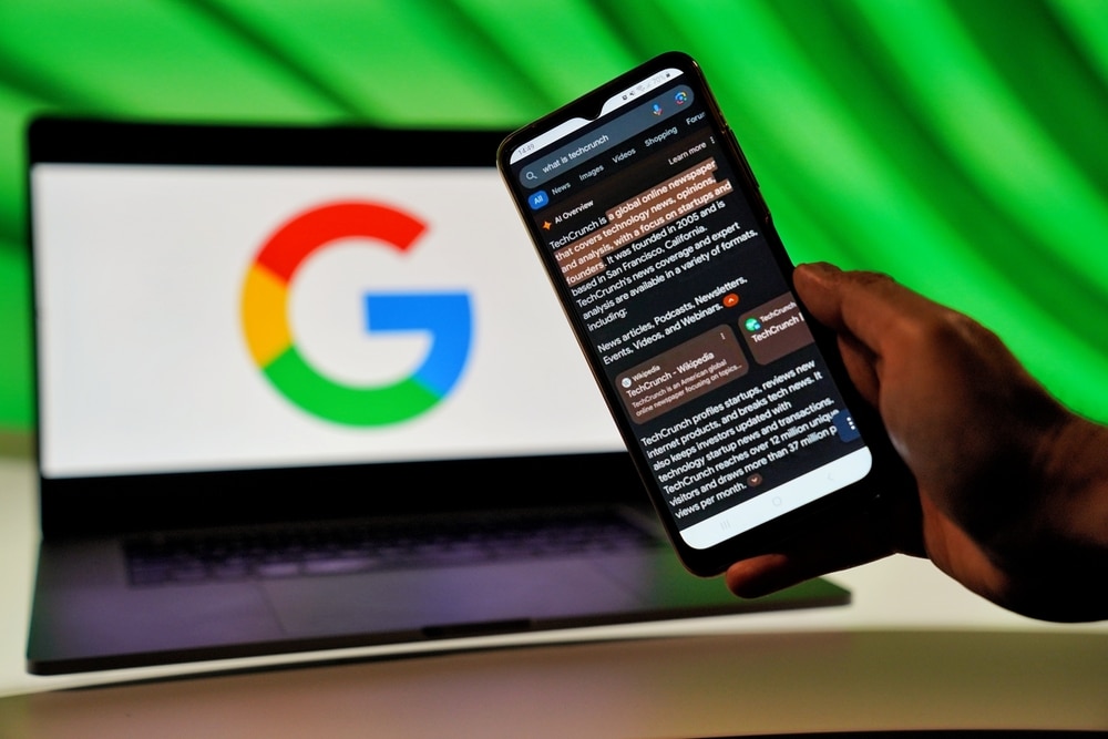 AI Overview på mobil med Laptop med Google-logo i bakgrunnen